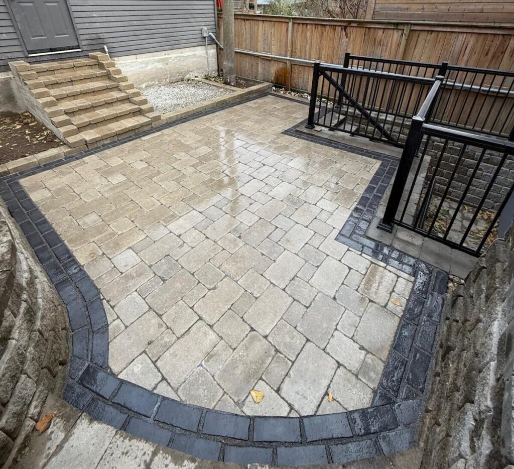 Backyard interlock patio with charcoal border and black railing